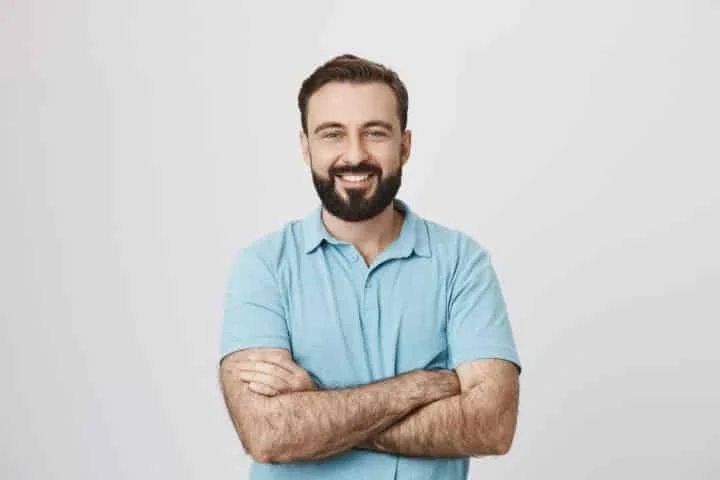 homem sorridente com barba bem cuidada, vestindo uma camisa social, posando para uma fotografia com flash.