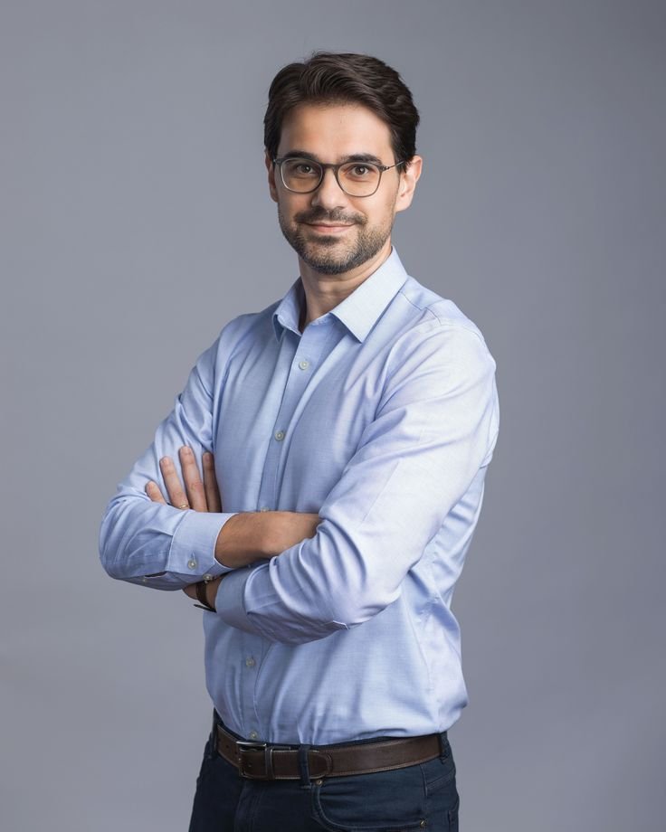 Retrato de uma pessoa sorridente usando óculos e roupa formal.